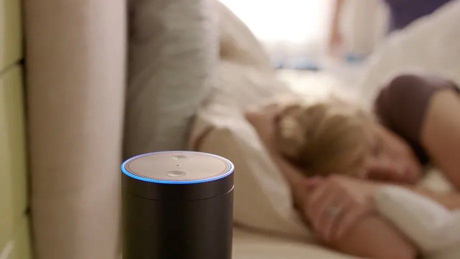 a woman is sleeping in a bed next to an amazon echo speaker .