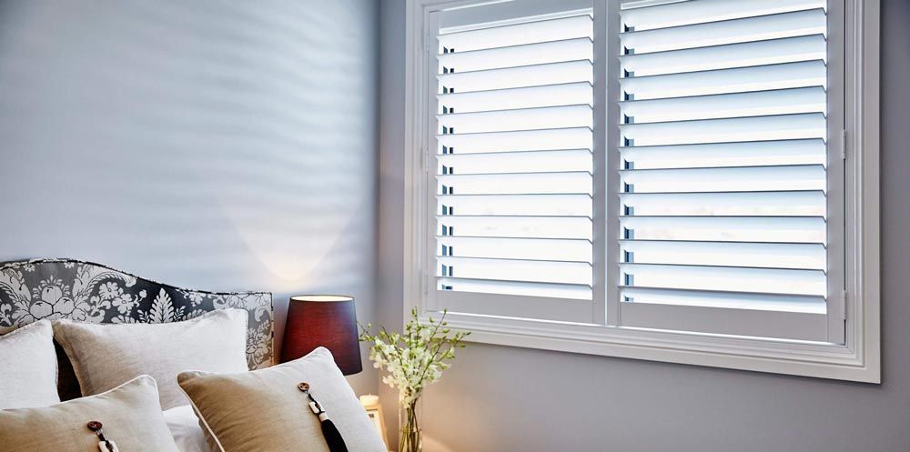 A bedroom with a bed and a window with white shutters