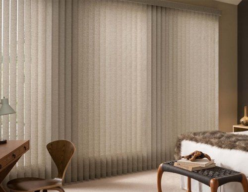 a bedroom with a large bed and a large window with vertical blinds on.