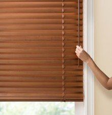 a person is holding a wand tilt wooden blind on a window .