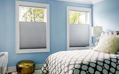 a bedroom with blue walls , a bed , two windows and honeycomb blinds installed by Affordable Blind Pros.