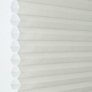 a close up of a white cellular 3/8 single cell blind on a window .