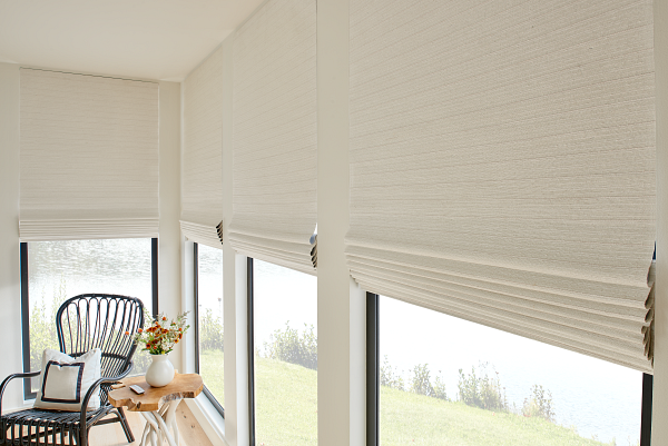 A room with a chair , table , and window with roman shades.