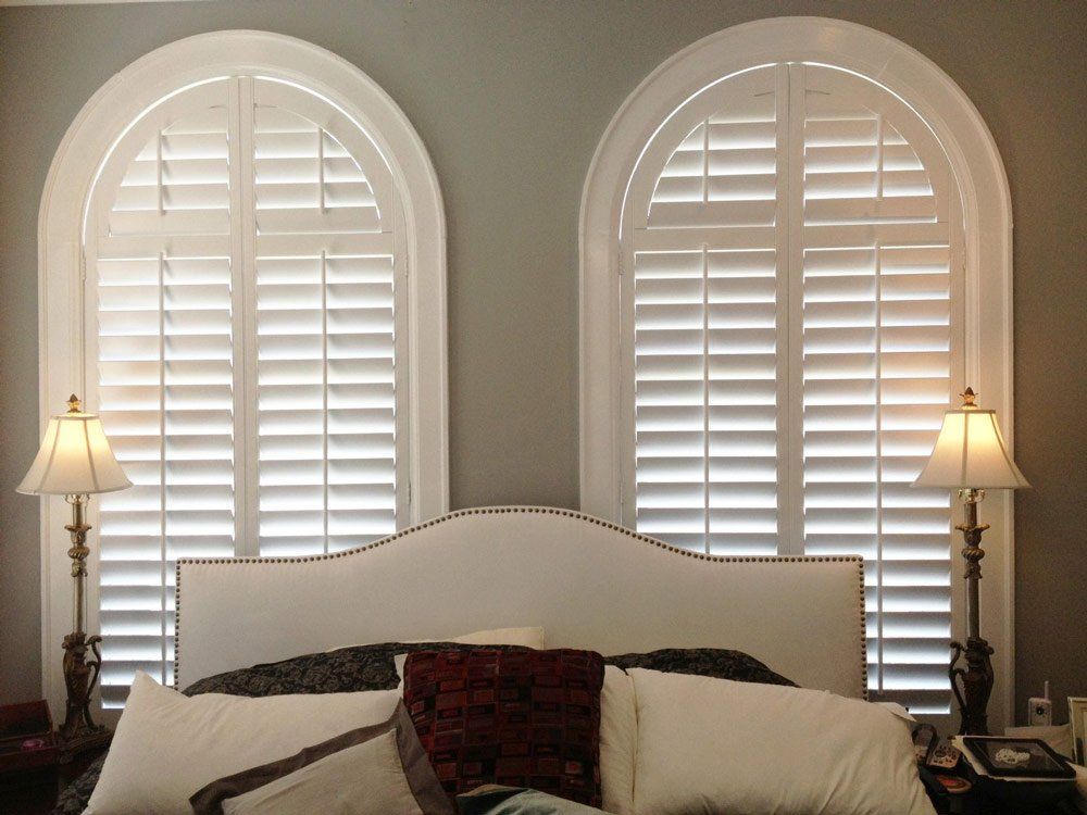 A bedroom with a bed and two arched windows with white shutters