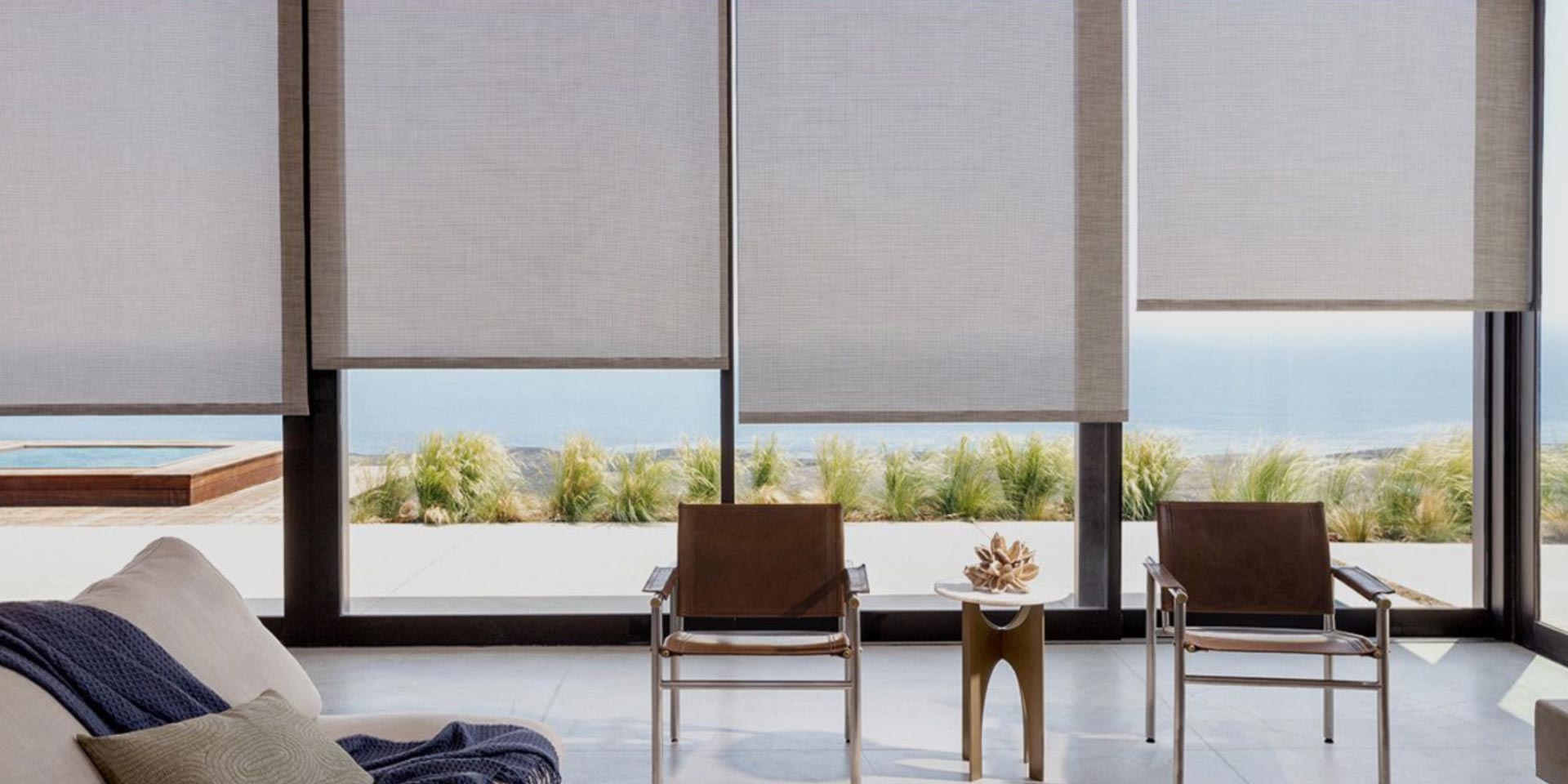 A living room with a couch , chairs and a table with a lots of windows with roller shades