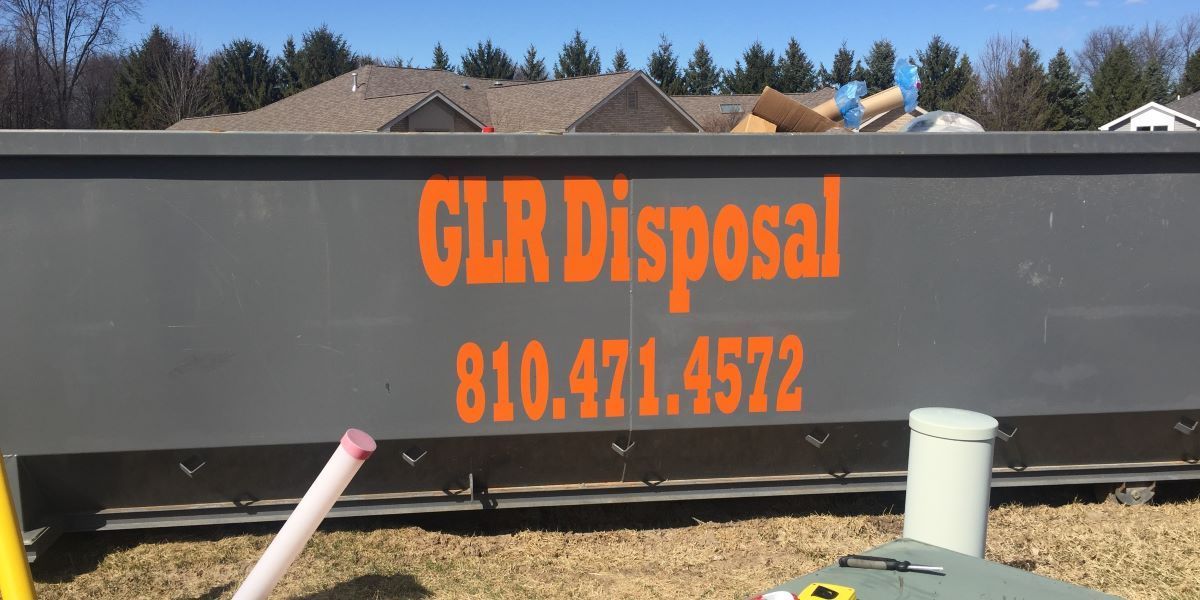 A large grey dumpster sits in a yard with the orange text 