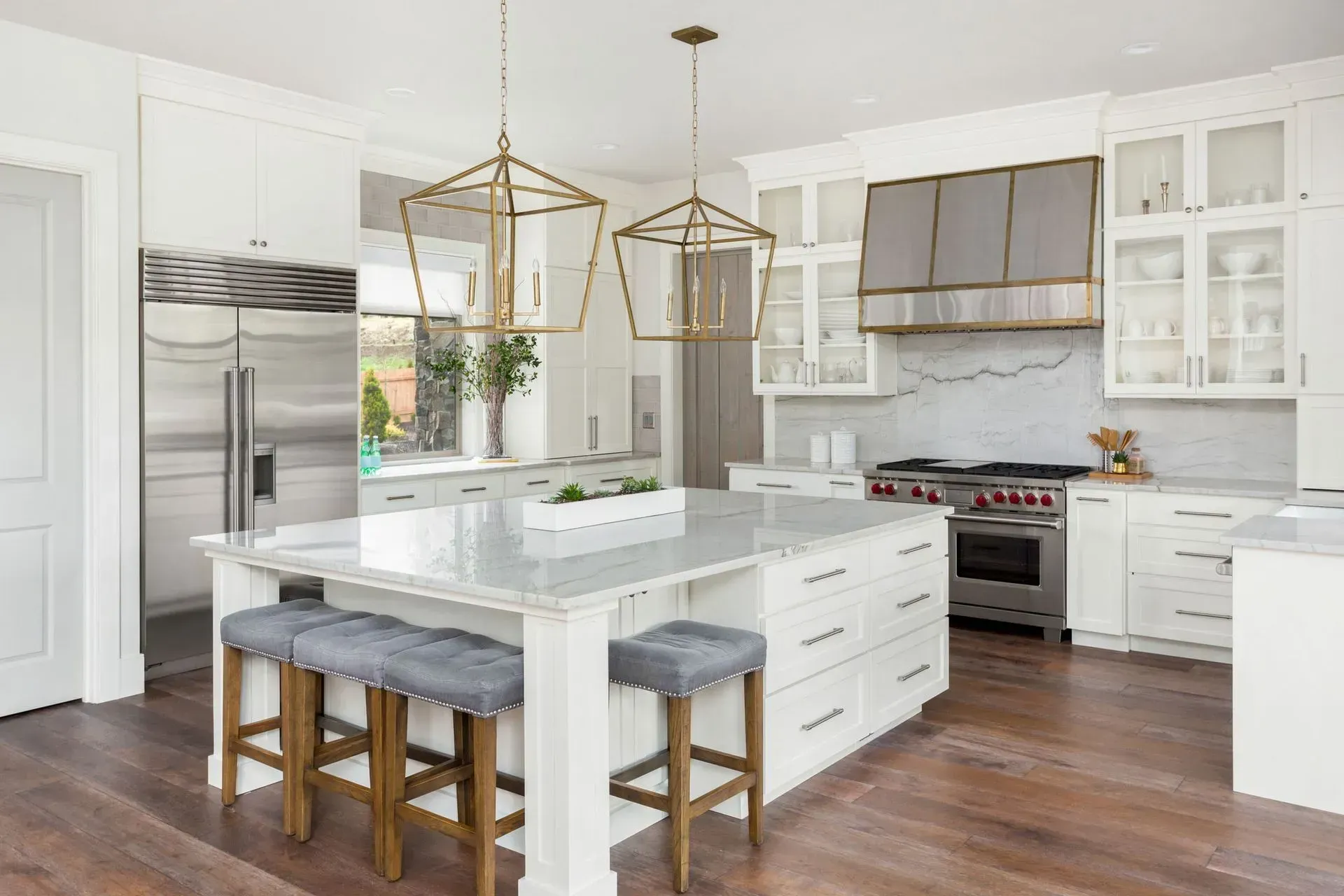 A kitchen with white cabinets , a large island , stools and a stove.