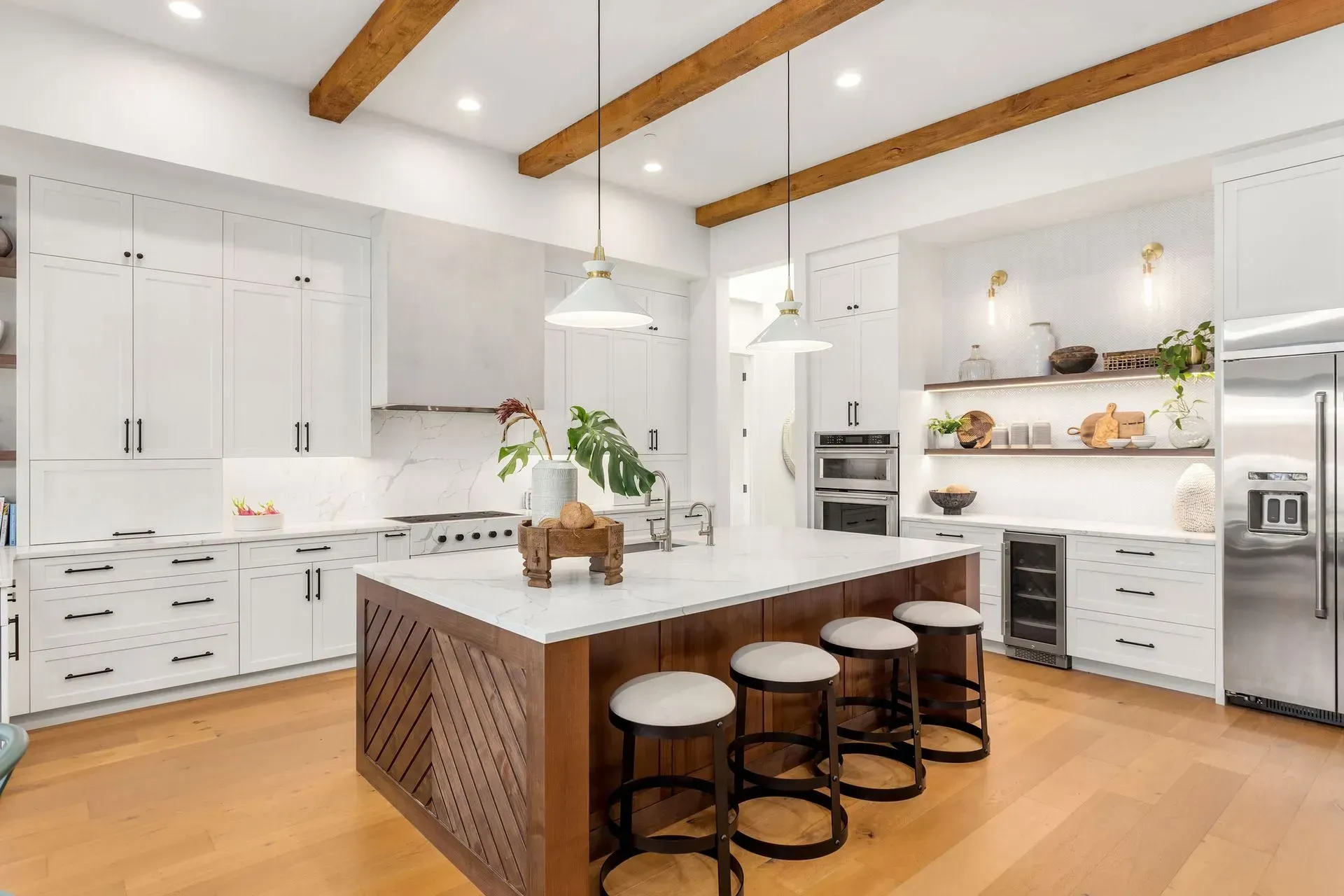 A kitchen with white cabinets , wooden floors , stools and a large island.