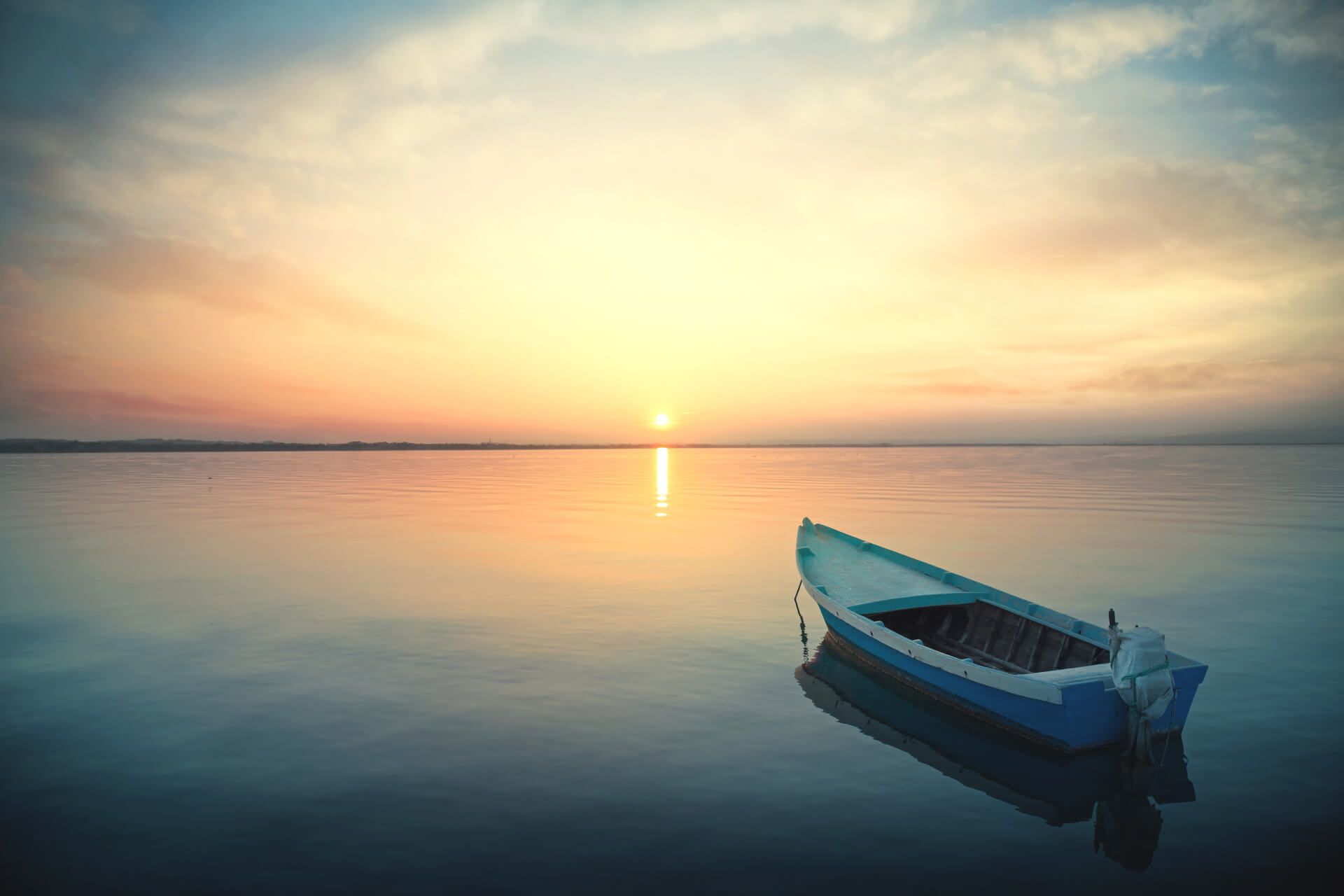 Een klein blauw bootje drijft op kalm water bij zonsondergang. De lucht weerspiegelt in de stilte.