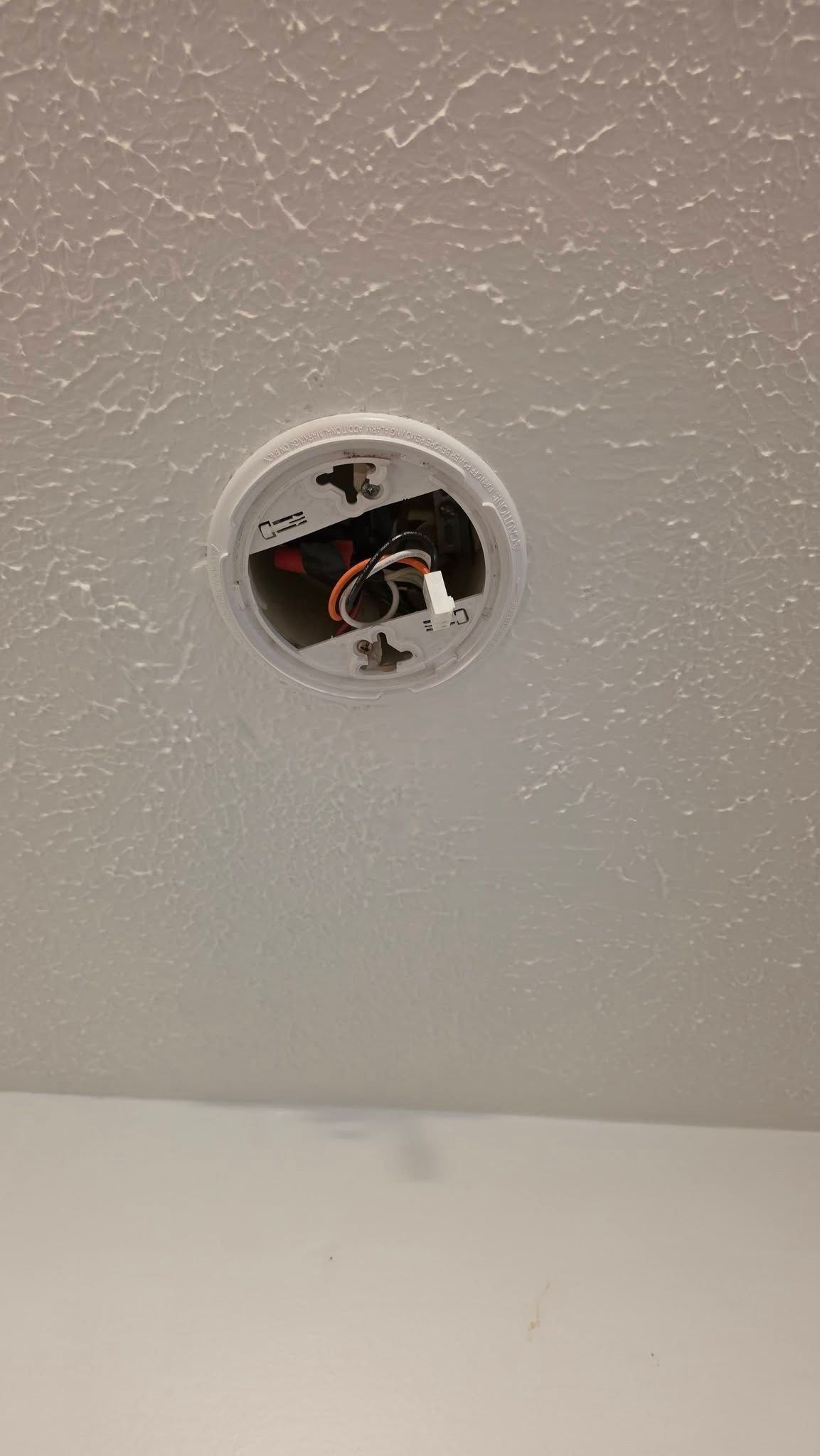 Ceiling-mounted smoke detector with an exposed wiring opening in a white textured ceiling