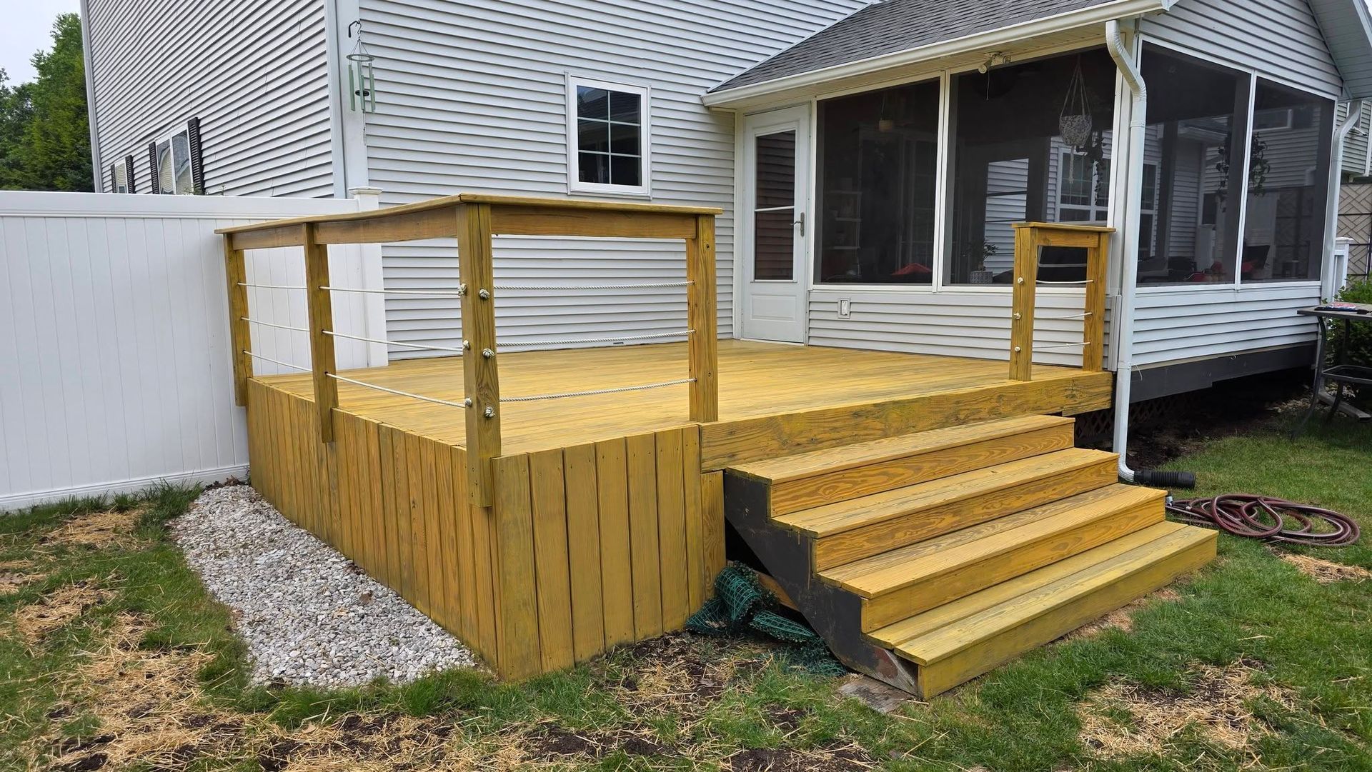 Wooden backyard deck with steps and railings beside a house, bordered by white privacy fencing.