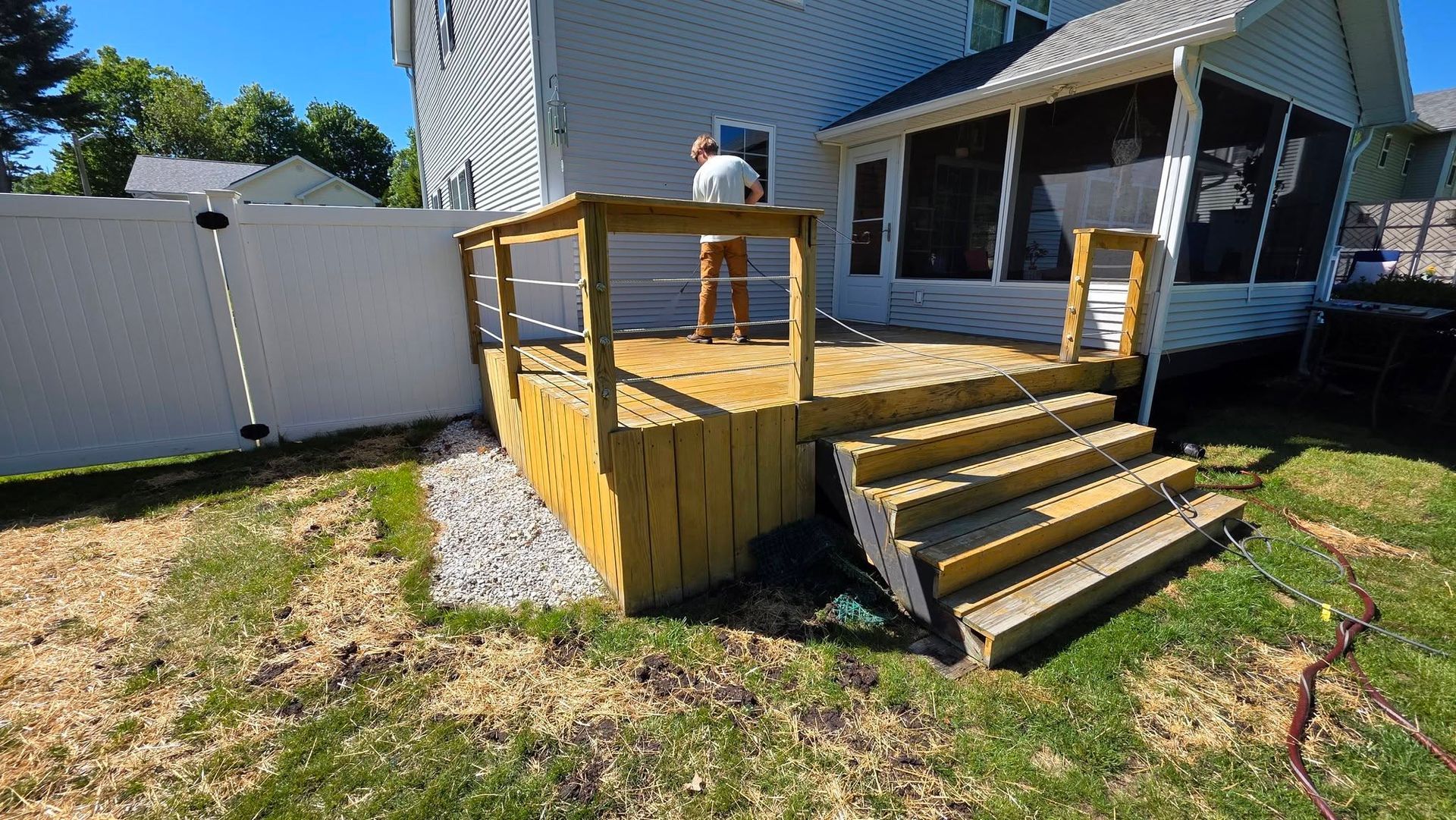 Wooden backyard deck with steps beside a house and white fence in sunny grass yard