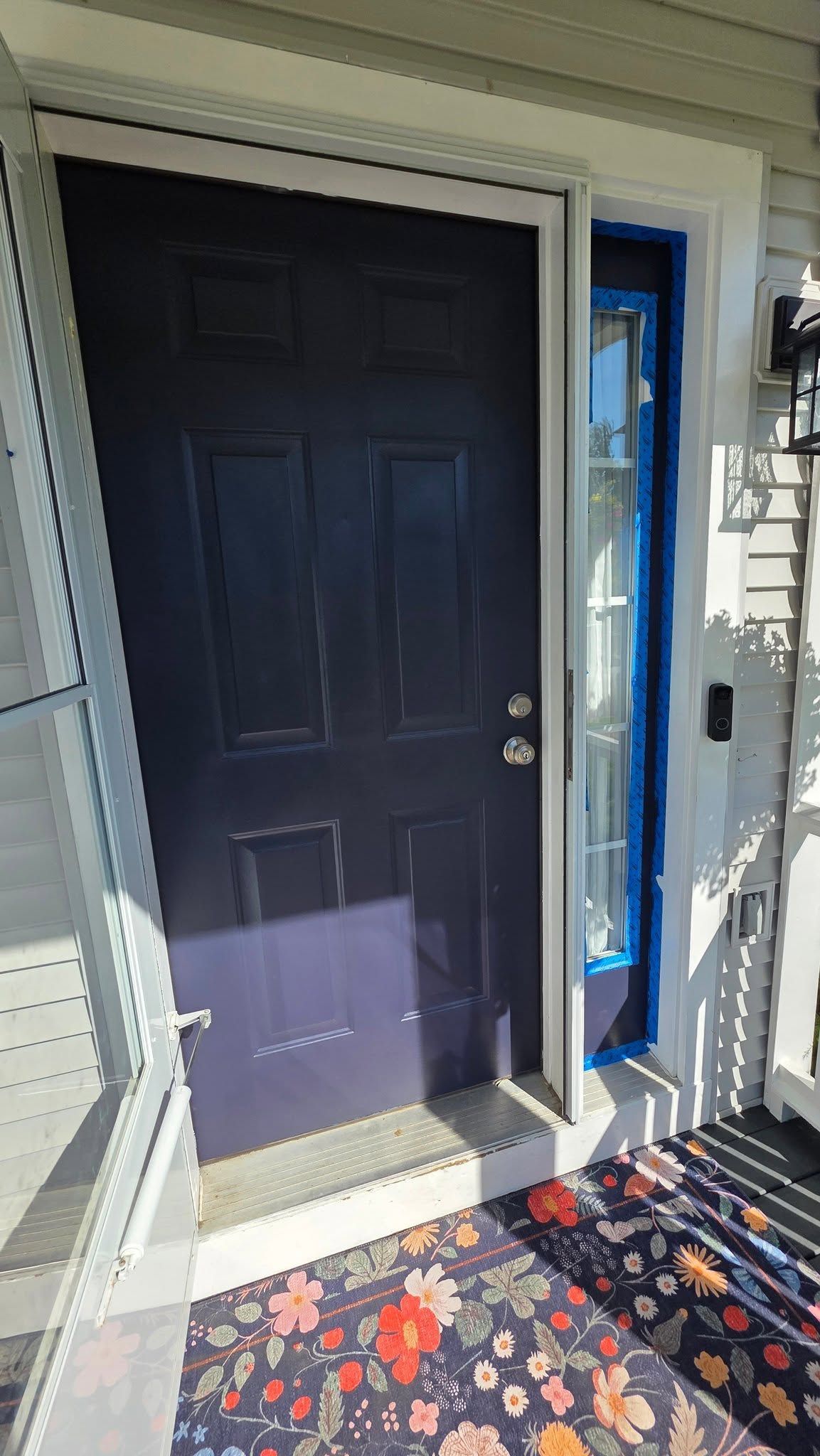 Front porch with a black door, narrow glass sidelight, and patterned outdoor rug.