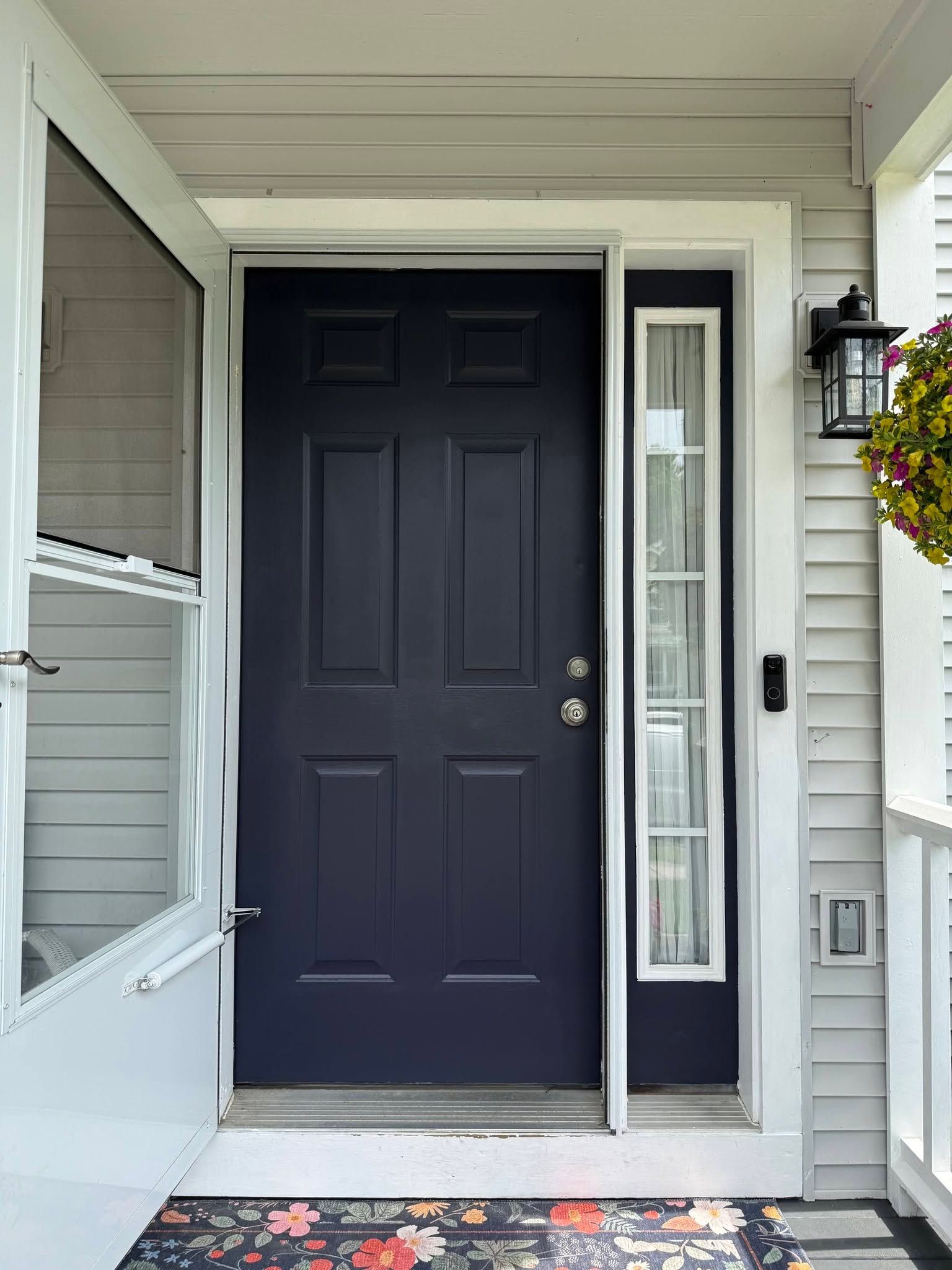 Front porch with dark navy front door, sidelights, and a white screen door open to the left.