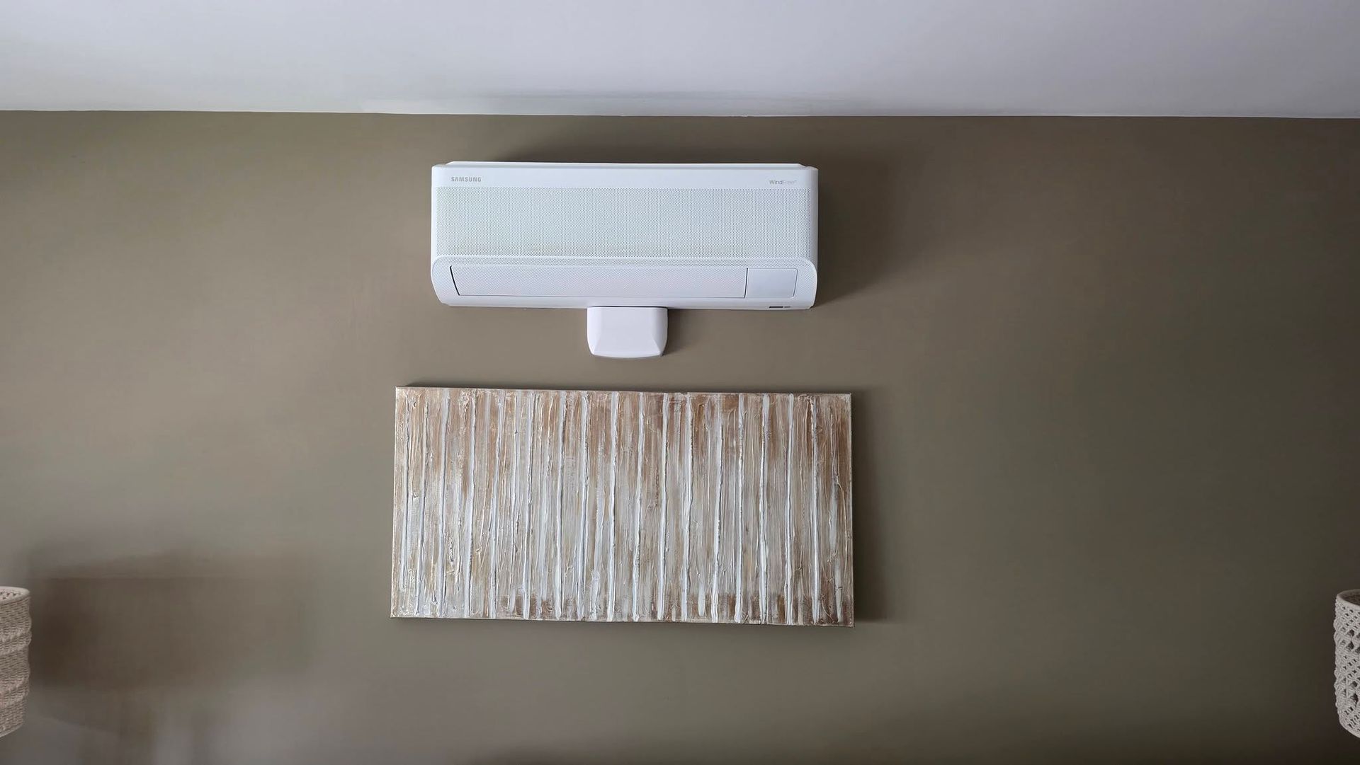 White wall-mounted air conditioner above a textured beige wall panel on a taupe wall