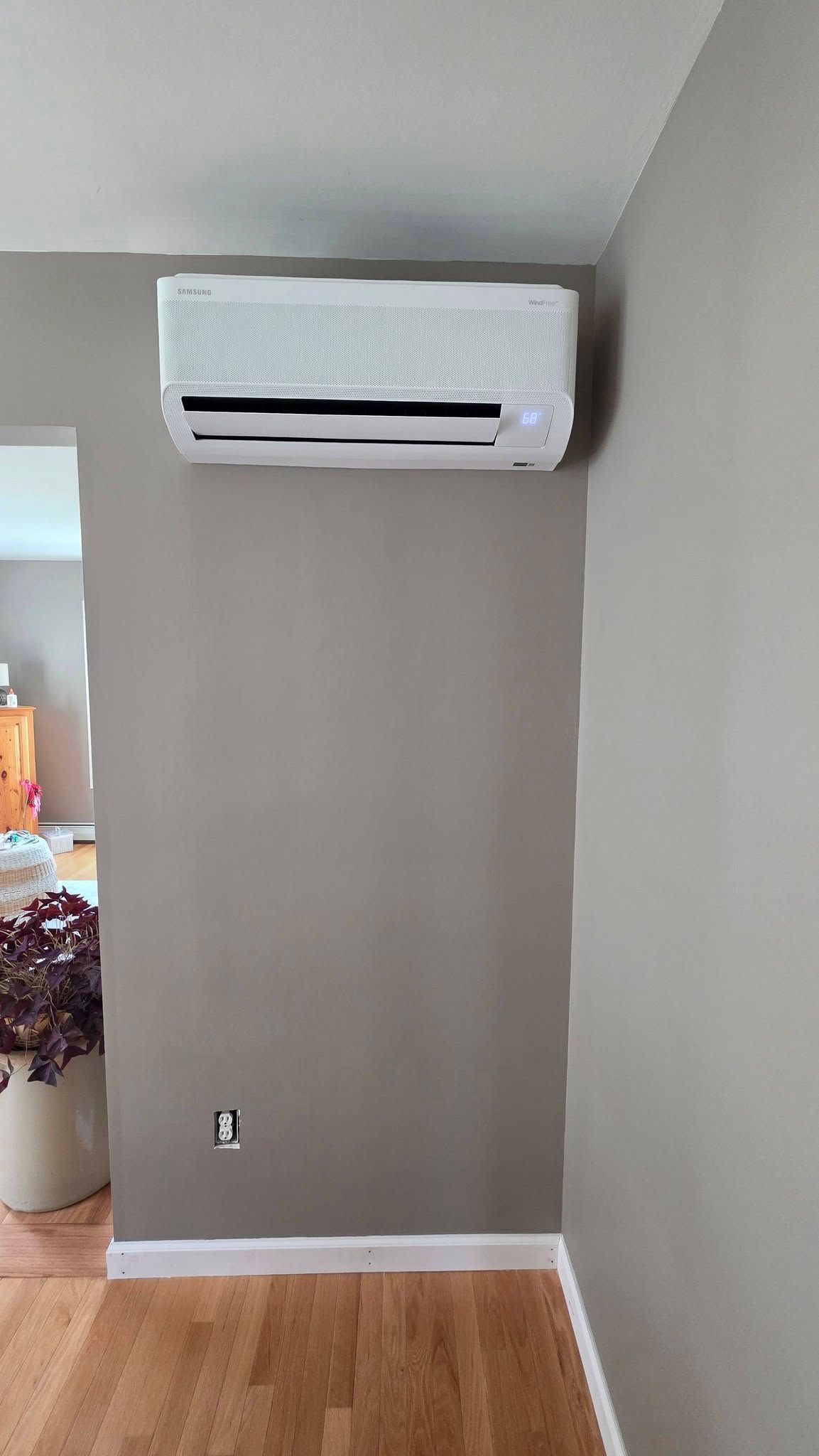White wall-mounted air conditioner above a gray accent wall in a room with hardwood floor