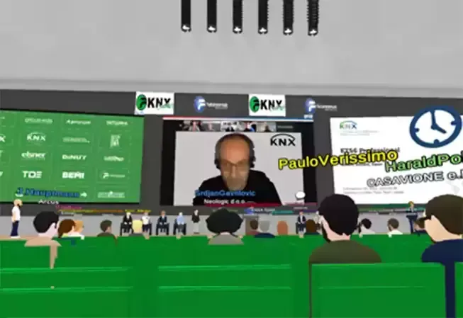 Virtual conference with speaker on screen and audience in a green-seated auditorium.