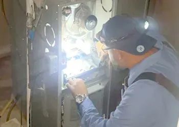 HVAC technician inspecting an appliance, using a headlamp.