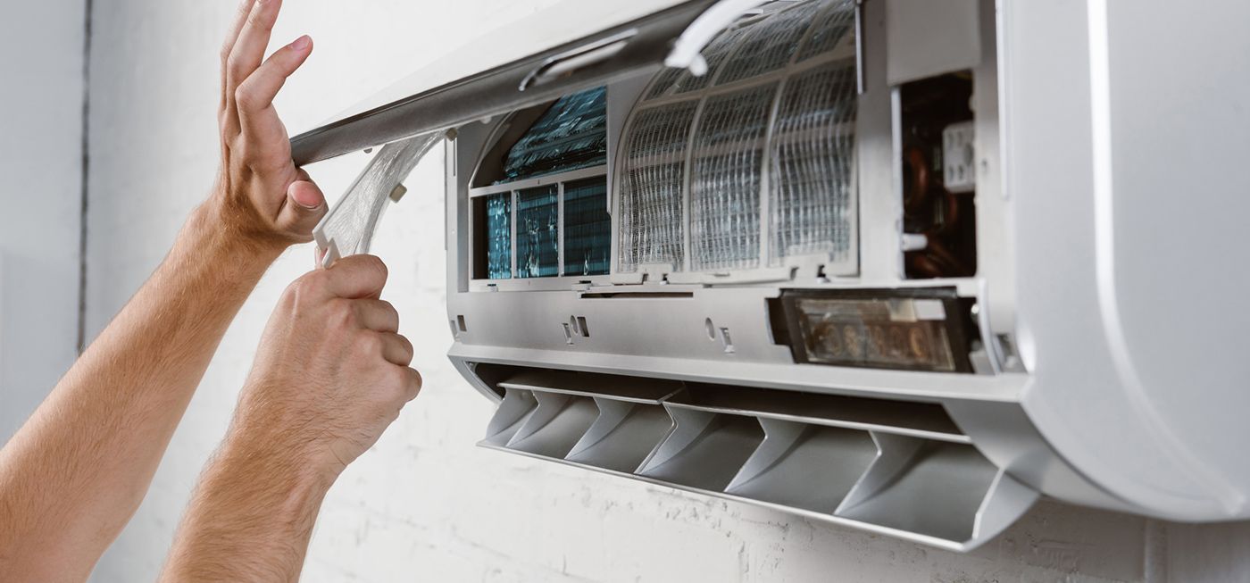 A person is cleaning an air conditioner with a brush.