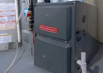 A goodman furnace is sitting in a basement next to a water heater.