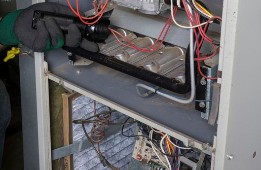 Open electrical panel with exposed wiring, cables, and gloves inside a gray cabinet