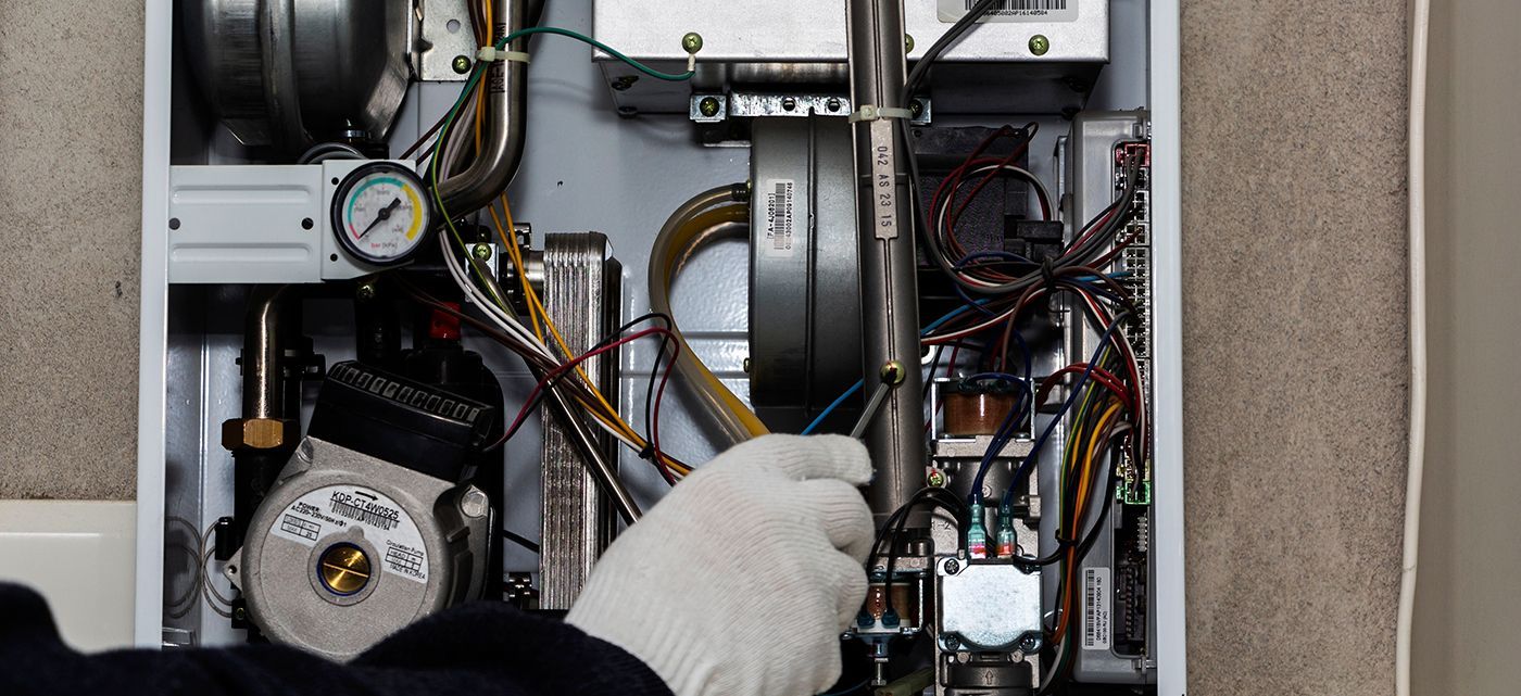 A person in white gloves working on the inner components of a heating system.