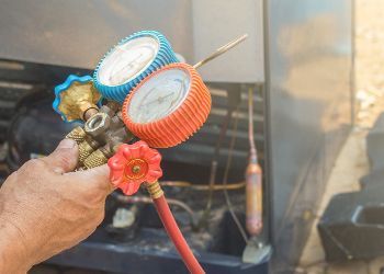 A person is holding a pressure gauge in front of a refrigerator.