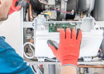 A man wearing red gloves is working on a boiler.
