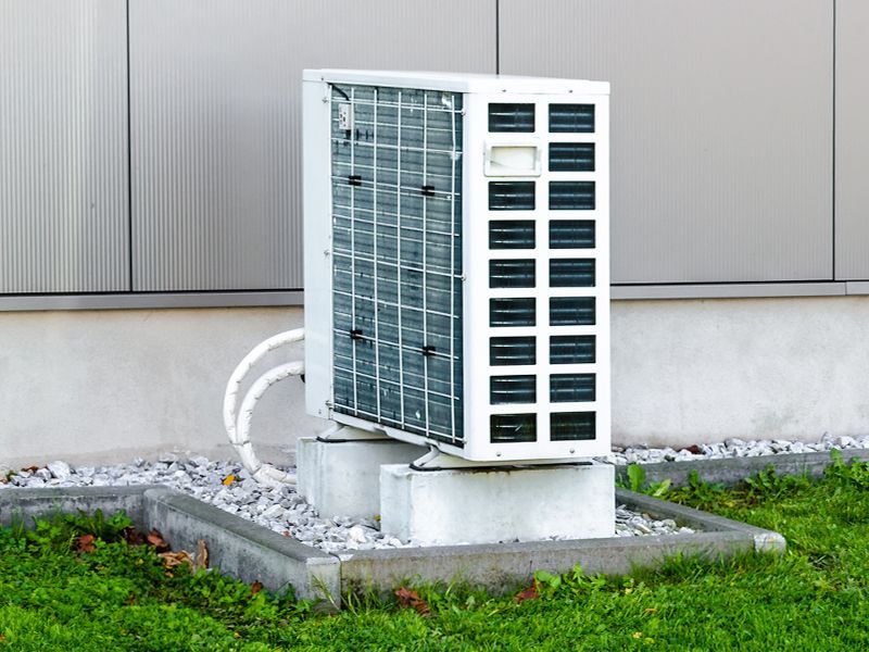 A white air conditioner is sitting on top of a concrete block in front of a building.