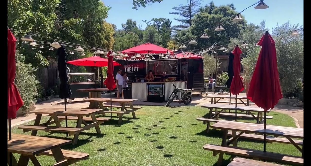 Food truck with table and umbrella setup on The Lot in Los Olivos.