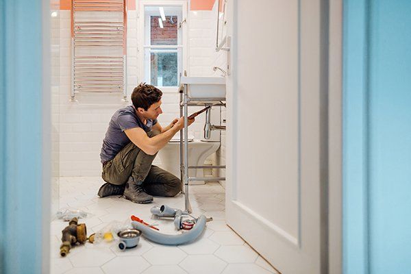 Man Fixing a Leak Under the Bathroom Sink — Croydon, PA — Jed Plumbing LLC Man Fixing a Leak Under the Bathroom Sink — Croydon, PA — Jed Plumbing LLC