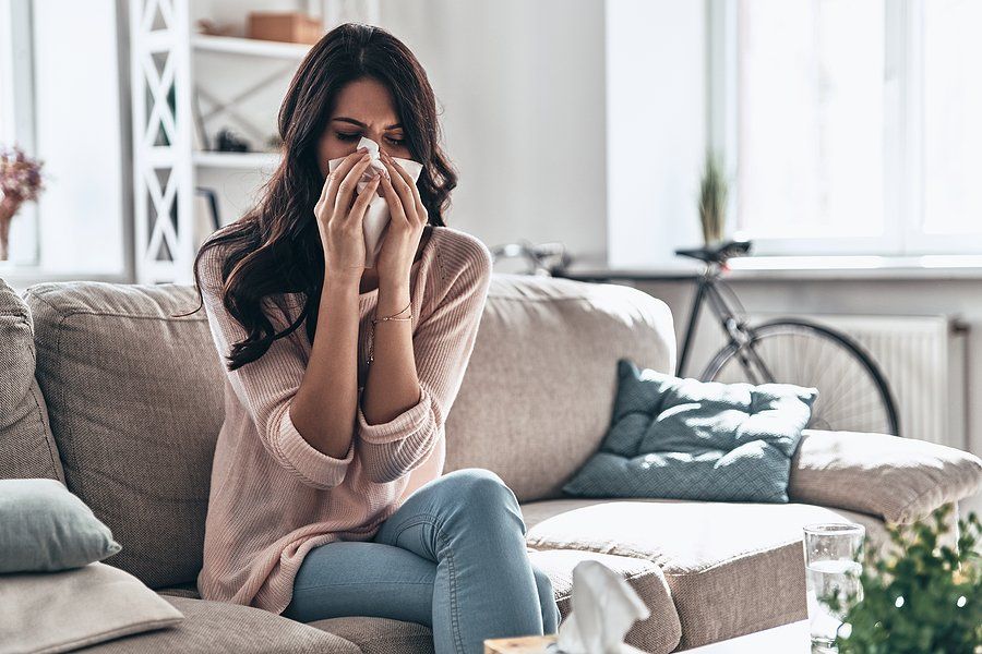 A woman is sitting on a couch blowing her nose into a tissue.