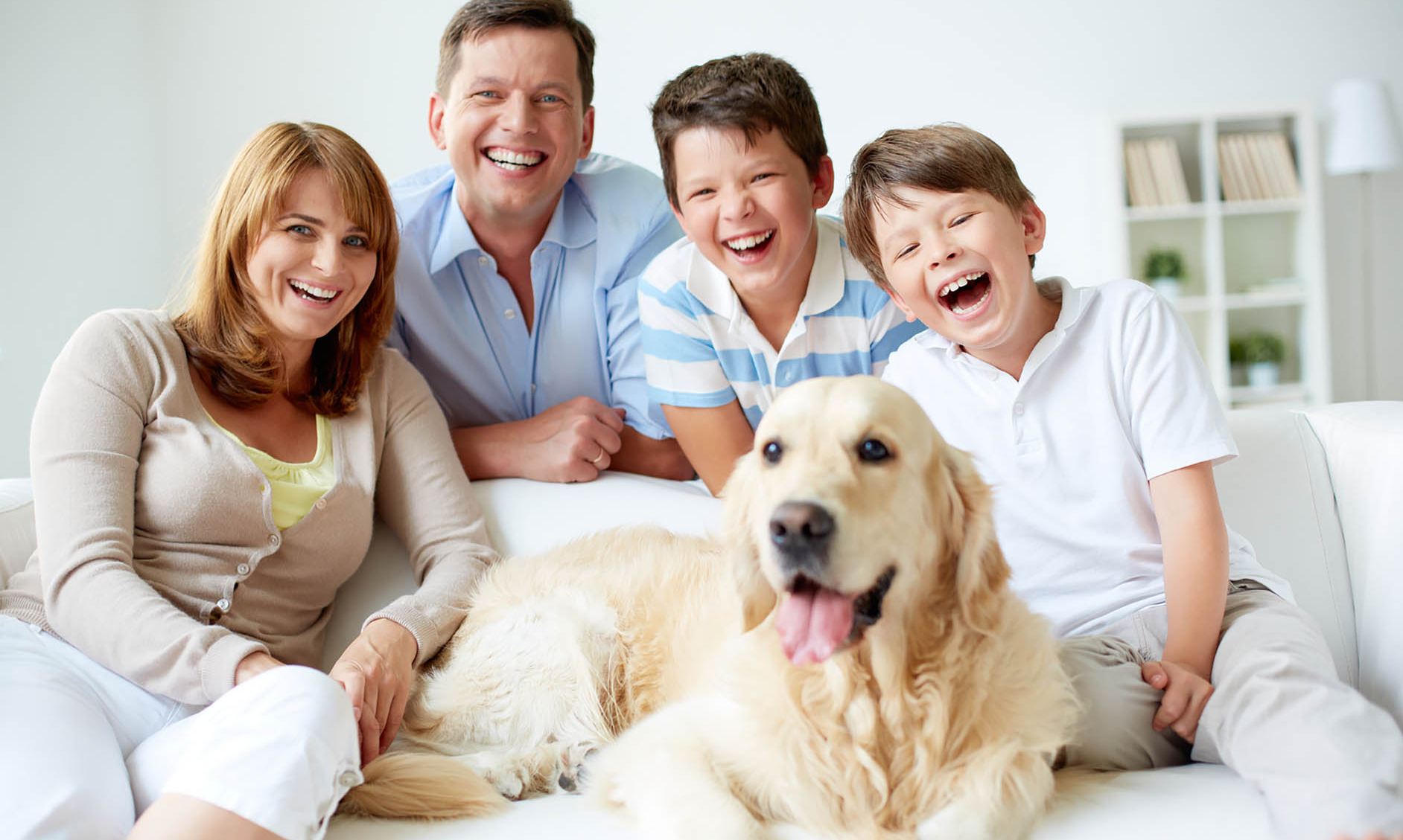 Family of four with a golden retriever, all smiling on a couch indoors.