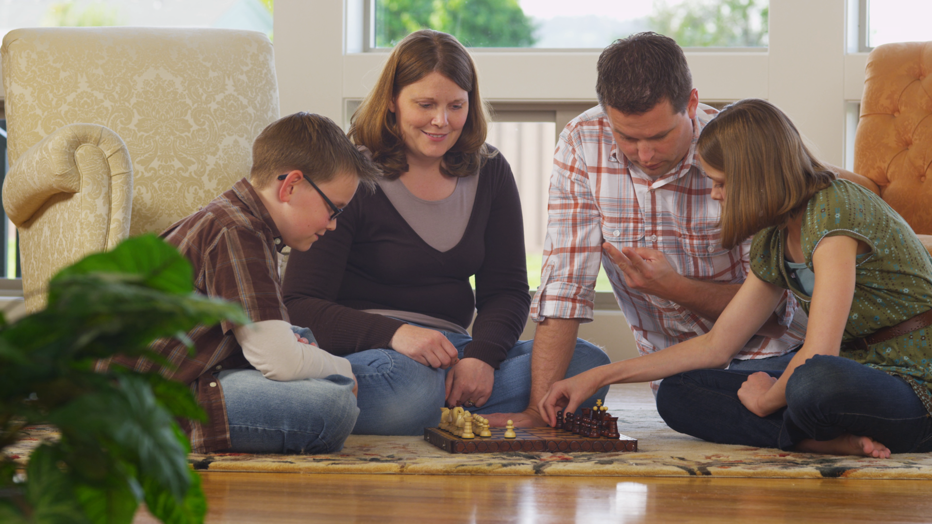 A family is sitting on the floor playing a game of chess.