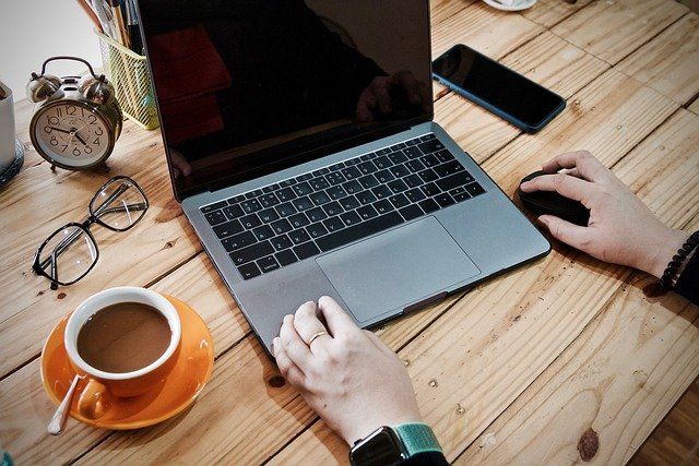 A person is typing on a laptop next to a cup of coffee.