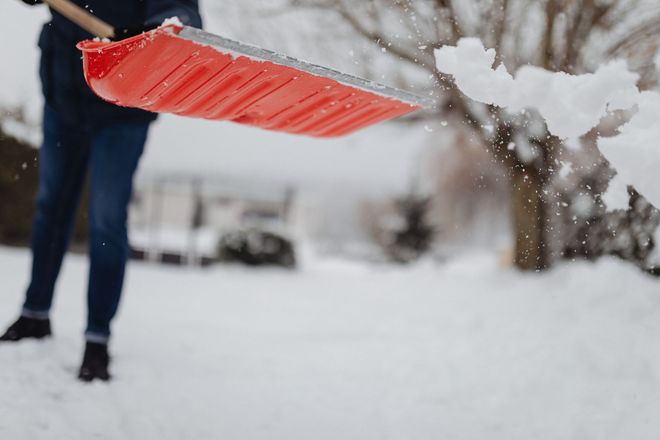 Person shoveling snow with a bright red shovel in a snowy yard