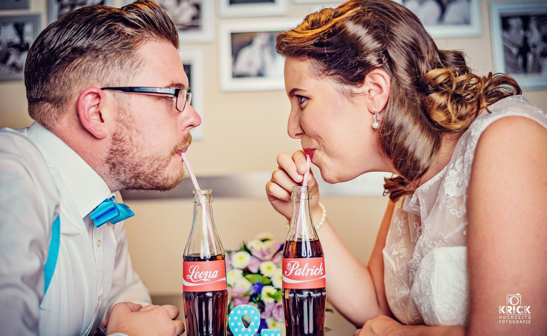 Zwei Personen sitzen sich gegenüber an einem Tisch und trinken Cola aus Glasflaschen mit Strohhalmen.