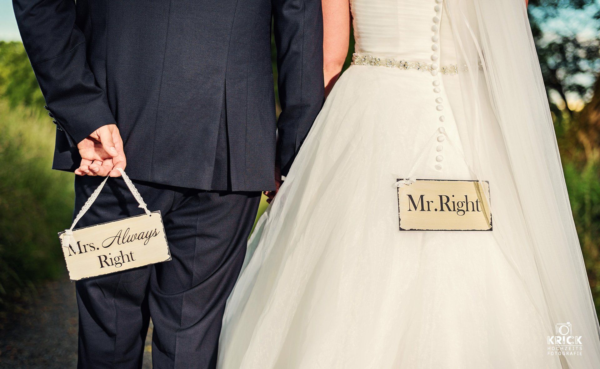 Braut und Bräutigam halten bei einer Hochzeit ein Schild und einen Brautrock mit den Aufschriften „Mr. Right“ und „Mrs. Right“.