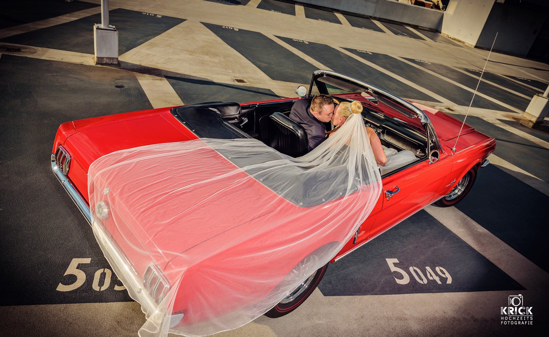 Ein rotes, klassisches Cabriolet, abgedeckt mit einer durchscheinenden rosa Plane, steht nachts auf einem Parkplatz.