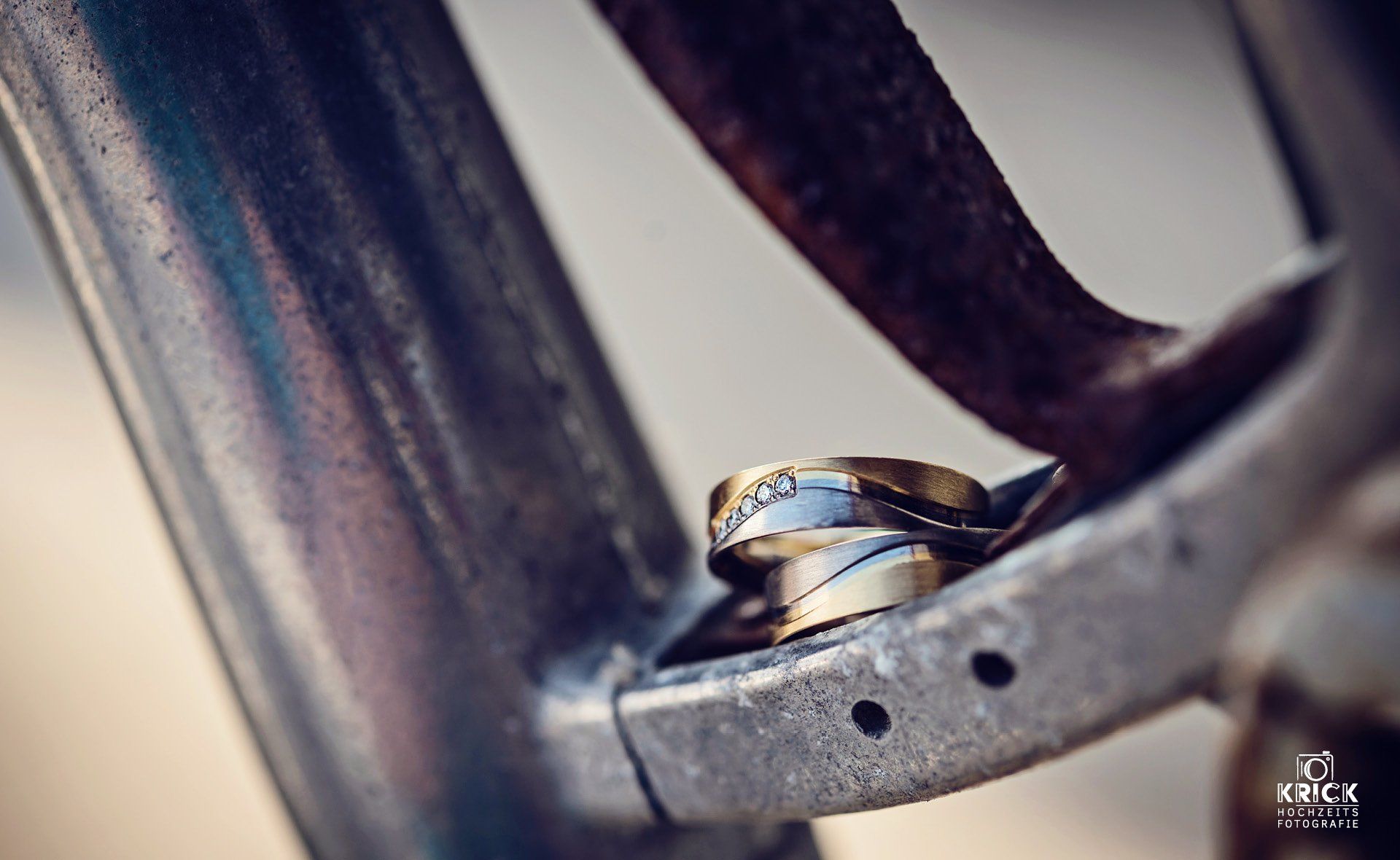 Zwei Eheringe auf einer Metalloberfläche, einer aus Gold und einer aus Silber mit Diamanten.