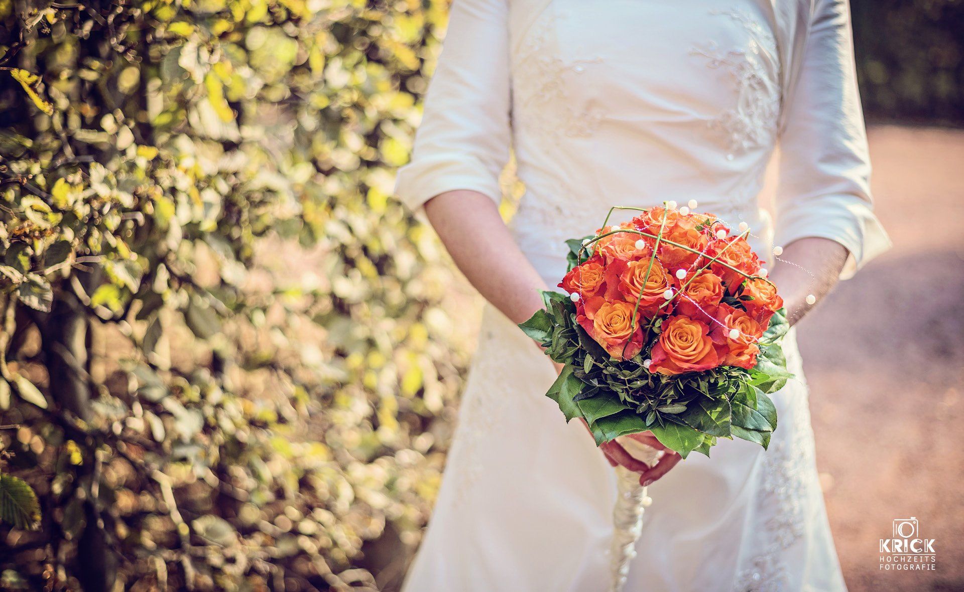 Person in einem weißen Kleid, die im Freien einen Strauß orangefarbener und roter Blumen hält