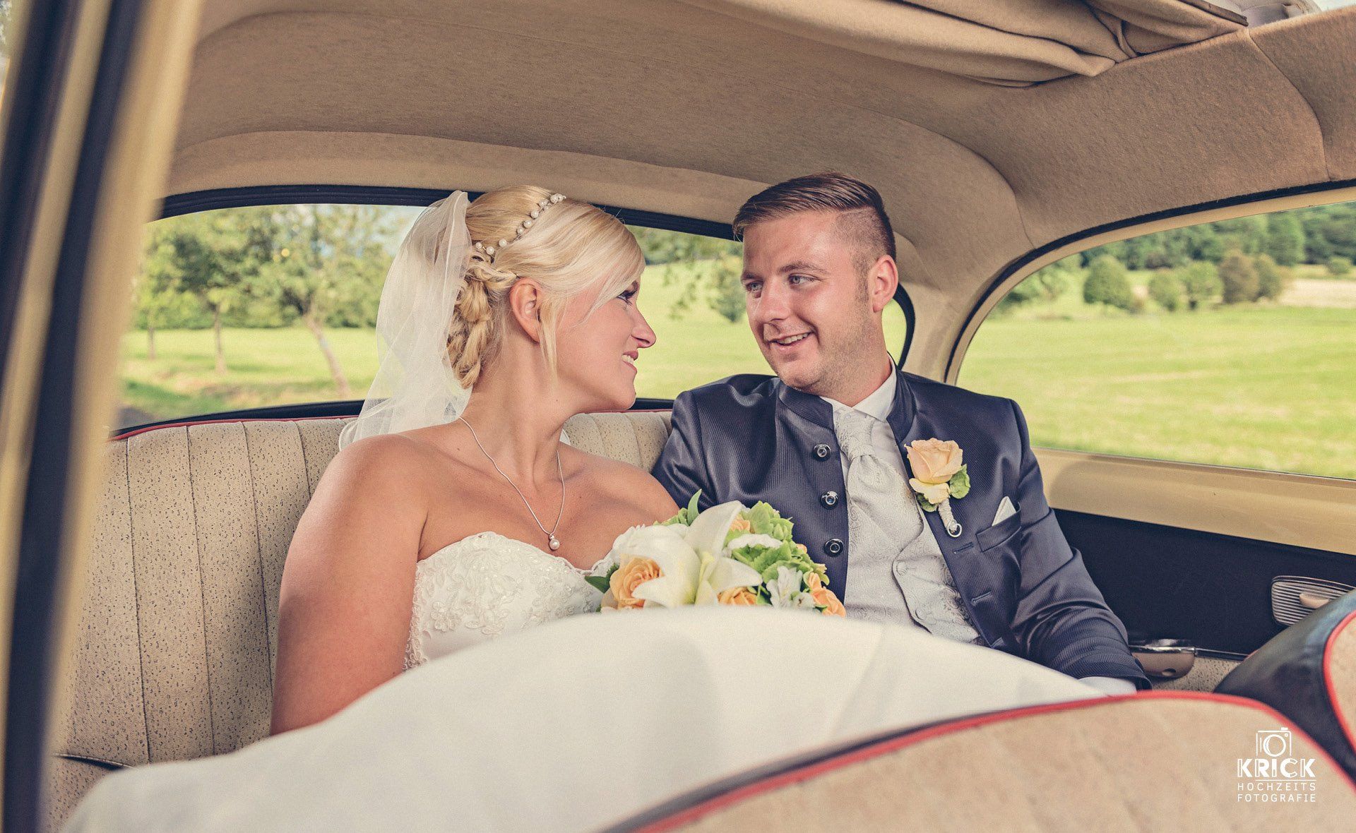 Braut und Bräutigam lächeln an ihrem Hochzeitstag in einem Oldtimer