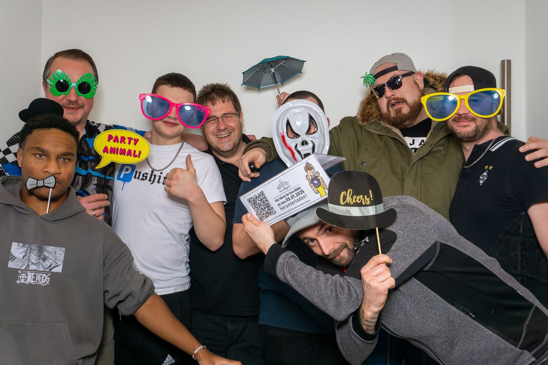 Eine Gruppe von Menschen posiert drinnen mit verspielten Masken, Requisiten und bunten Spaßbrillen.