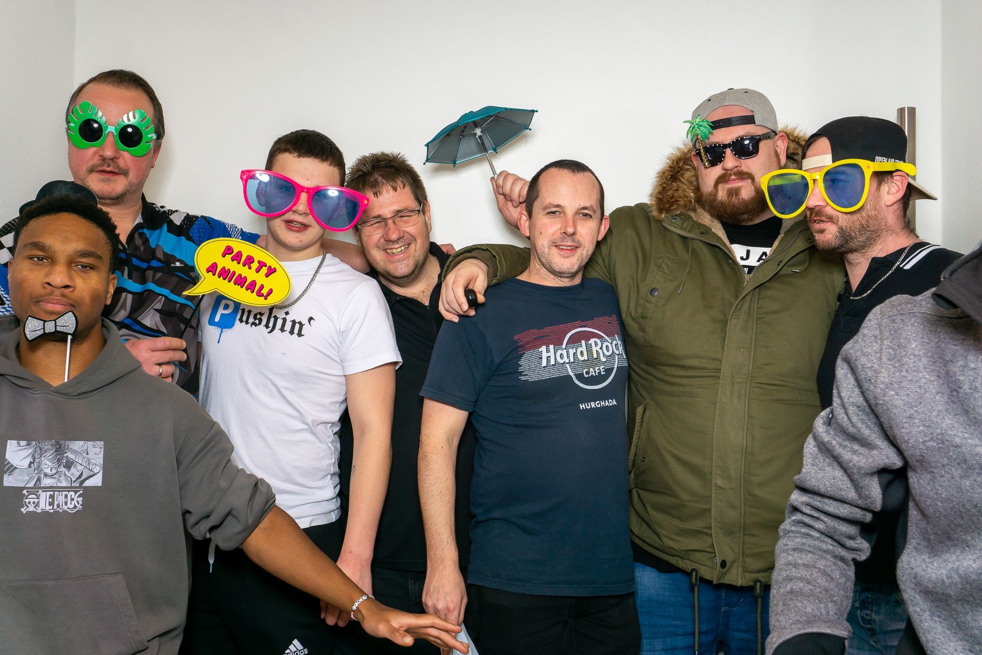 Eine Gruppe von Menschen posiert in einem Innenraum, einige tragen bunte, übergroße Spaßbrillen.