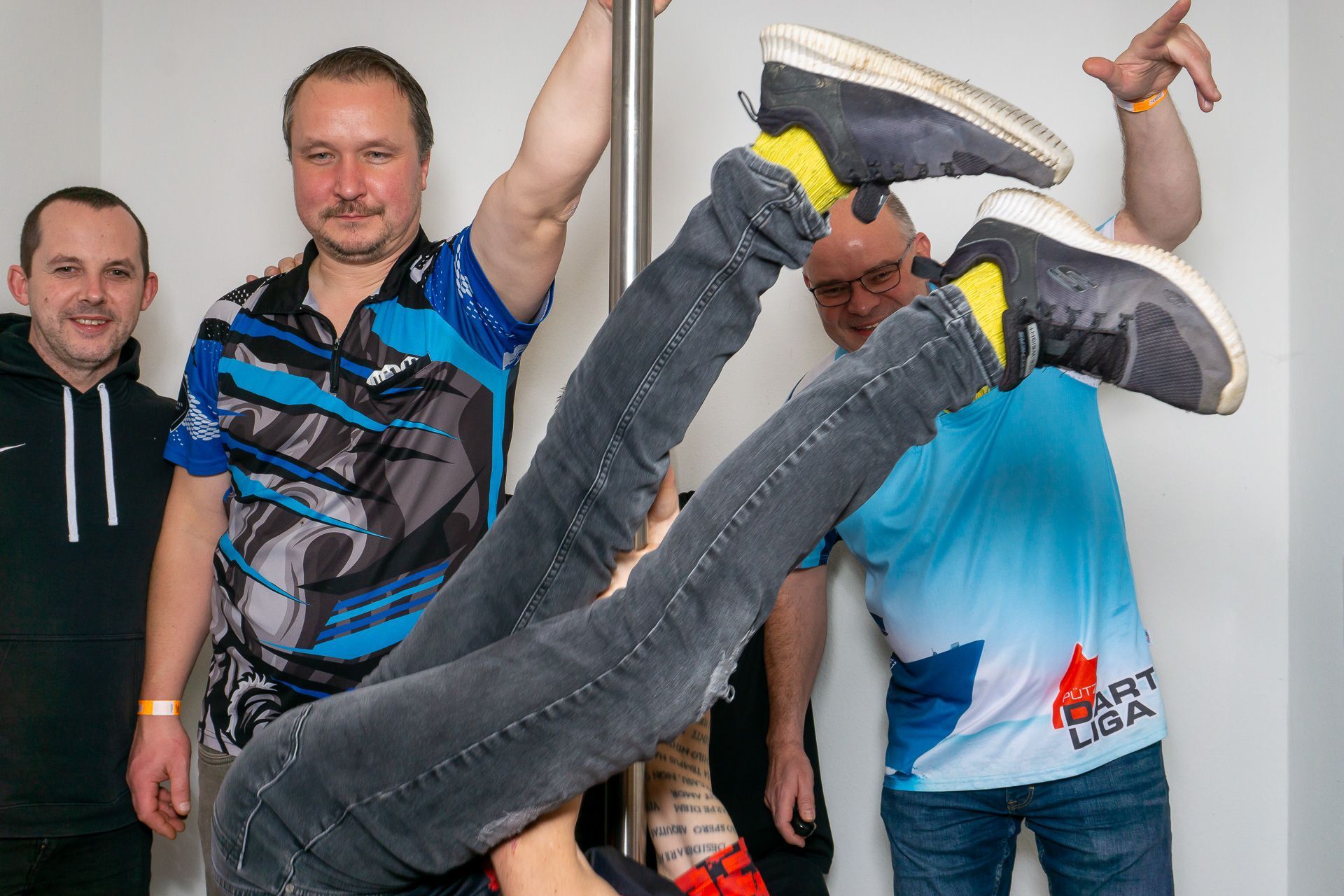 Vier Männer in einem Innenraum, einer macht einen spielerischen Handstand, während die anderen posieren und lächeln.