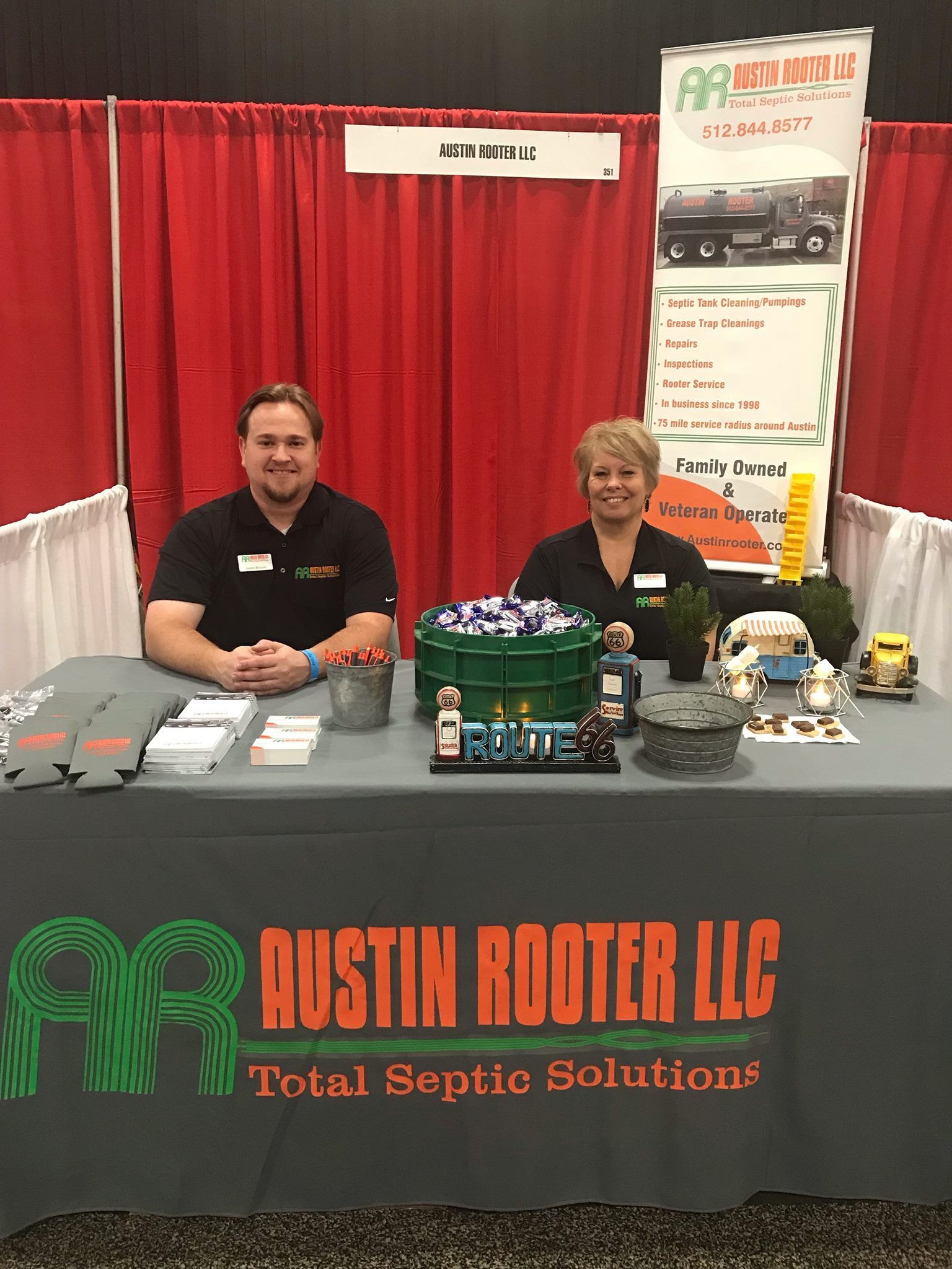 A man and a woman are sitting at a table with a sign that says austin rooter llc total septic solutions.