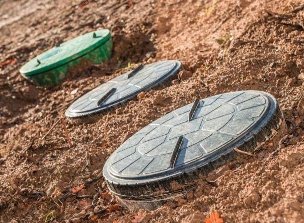 Three septic tank lids are sitting on top of a dirt field.