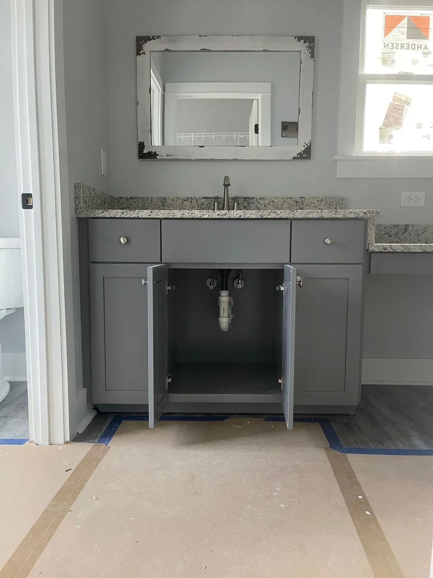 Gray bathroom vanity with open doors, light gray walls, and a distressed white mirror.
