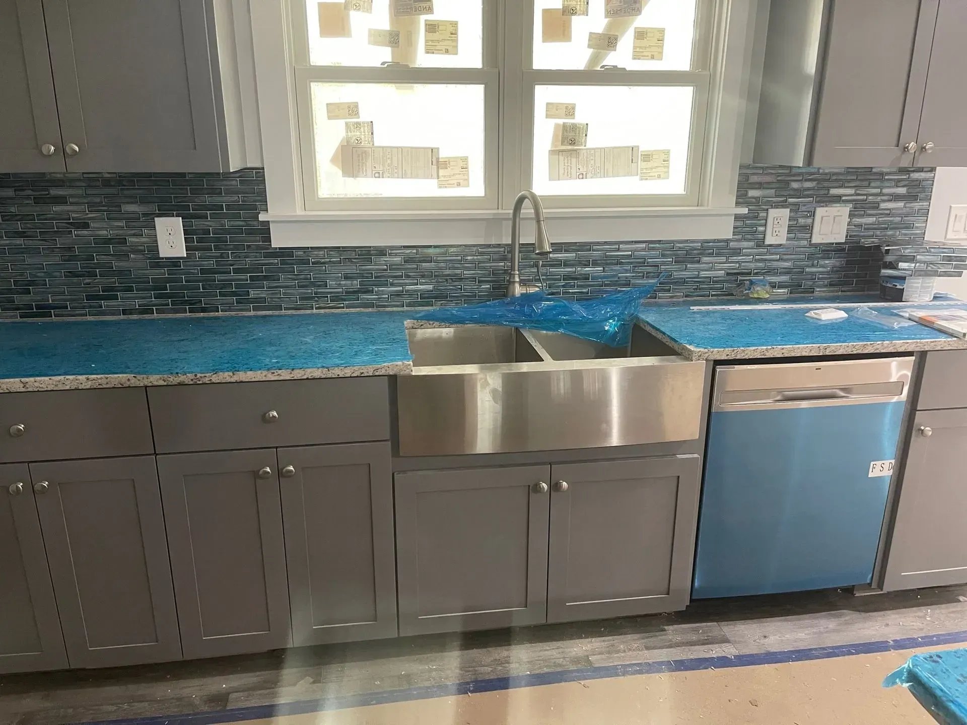 Gray kitchen cabinets with stainless steel sink and dishwasher, blue backsplash, and blue-covered countertops.