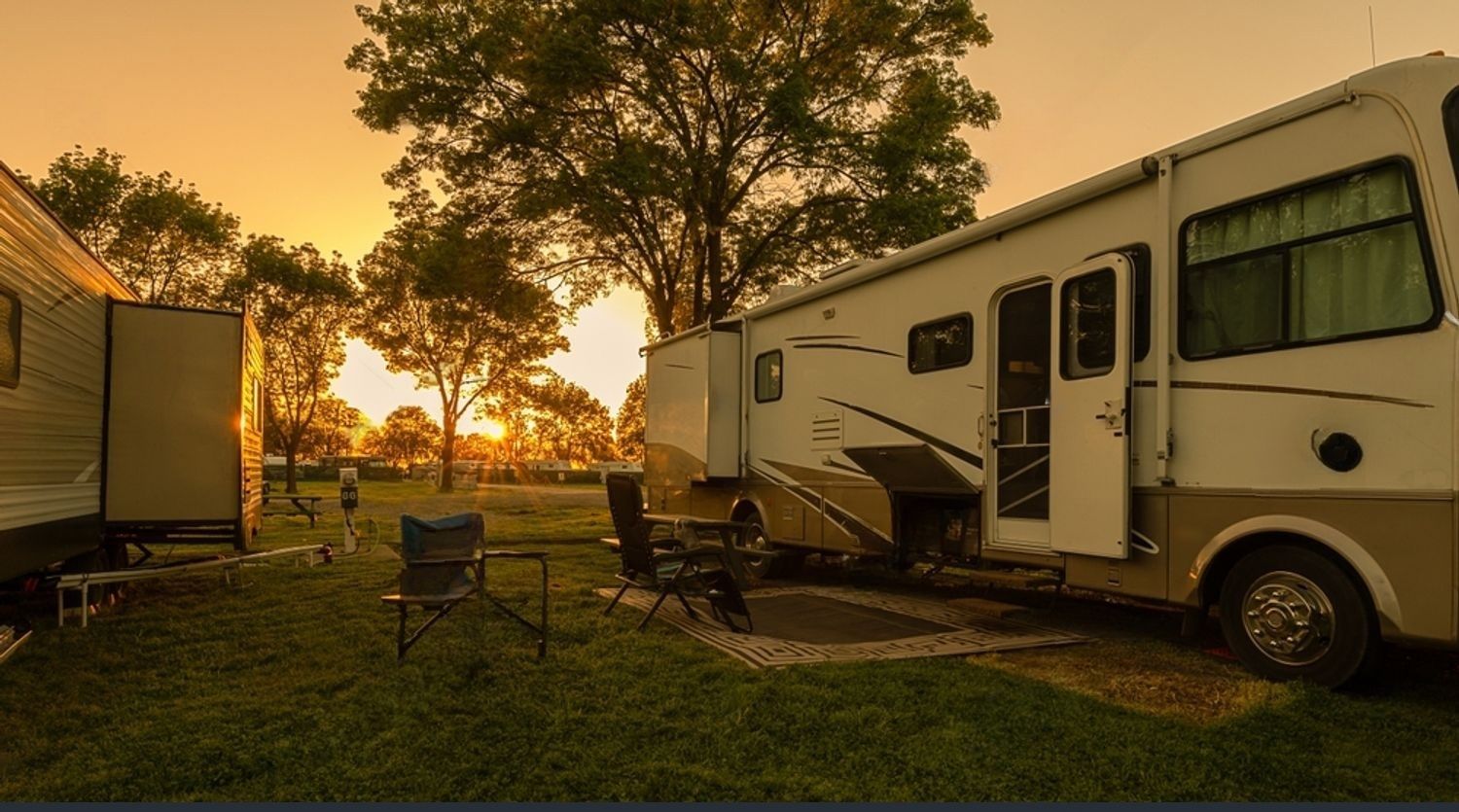 A rv is parked in a grassy field at sunset.